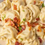 Pierogi ruskie z nadzieniem ziemniaczanym i twarogiem, podane z sosem cebulowym.